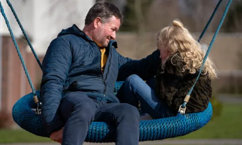 pleegvader en kind in hangschommel kijkend naar elkaar